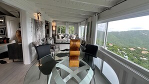 Ein modernes Wohnzimmer mit einem Glastisch, einer Couch und Blick auf eine gebirgige Landschaft.