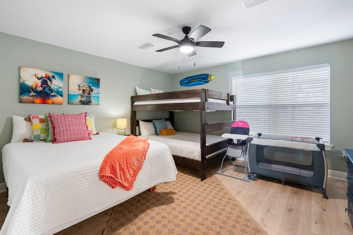Quarto com cama de solteiro, beliche, ventilador de teto, janela com persianas e cama para animais de estimação.