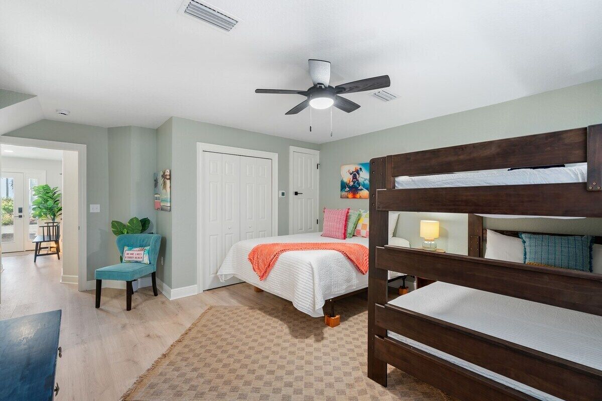 A bedroom with a bunk bed, a ceiling fan, a door, and a chair.
