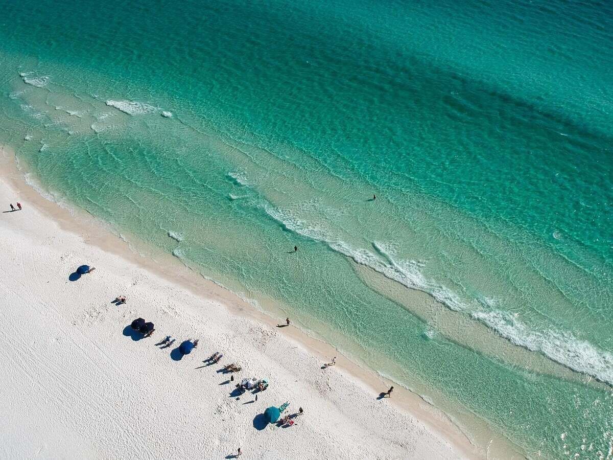 A beach with clear turquoise water, a sandy shore, and people sunbathing.