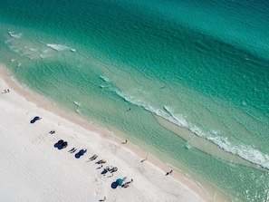 Uma praia com águas turquesa cristalinas, uma faixa de areia e pessoas se banhando ao sol.