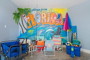 A room with a mural of Florida, a beach chair, a blue folding chair, and a blue storage bin.