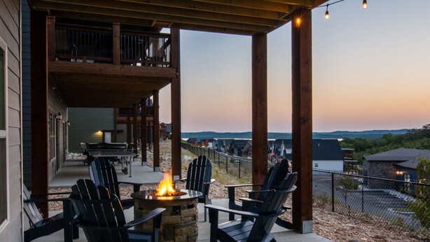 A covered outdoor seating area with Adirondack chairs and a fire pit, overlooking a scenic landscape. - Twisty slide, Lake view, Hot tub, Indoor pool, Fire pit | Skye Retreat (Branson)