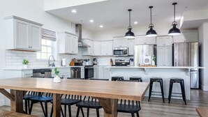 A modern kitchen with white cabinetry, stainless steel appliances, and a wooden dining table with black chairs. - Twisty slide, Lake view, Hot tub, Indoor pool, Fire pit | Skye Retreat (Branson)