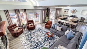 A spacious living area with a large sofa, two armchairs, a coffee table, and a dining table with chairs. There is a large window with curtains, a ceiling fan, and a Christmas tree. - Twisty slide, Lake view, Hot tub, Indoor pool, Fire pit | Skye Retreat (Branson)