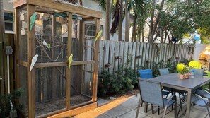 Una jaula de madera con varios compartimentos y un jardín vallado con sillas y una mesa.