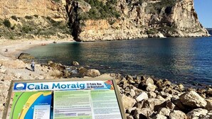 Uma praia rochosa com uma placa indicando Cala Moraig e El Poble Nou de Benitatxell.
