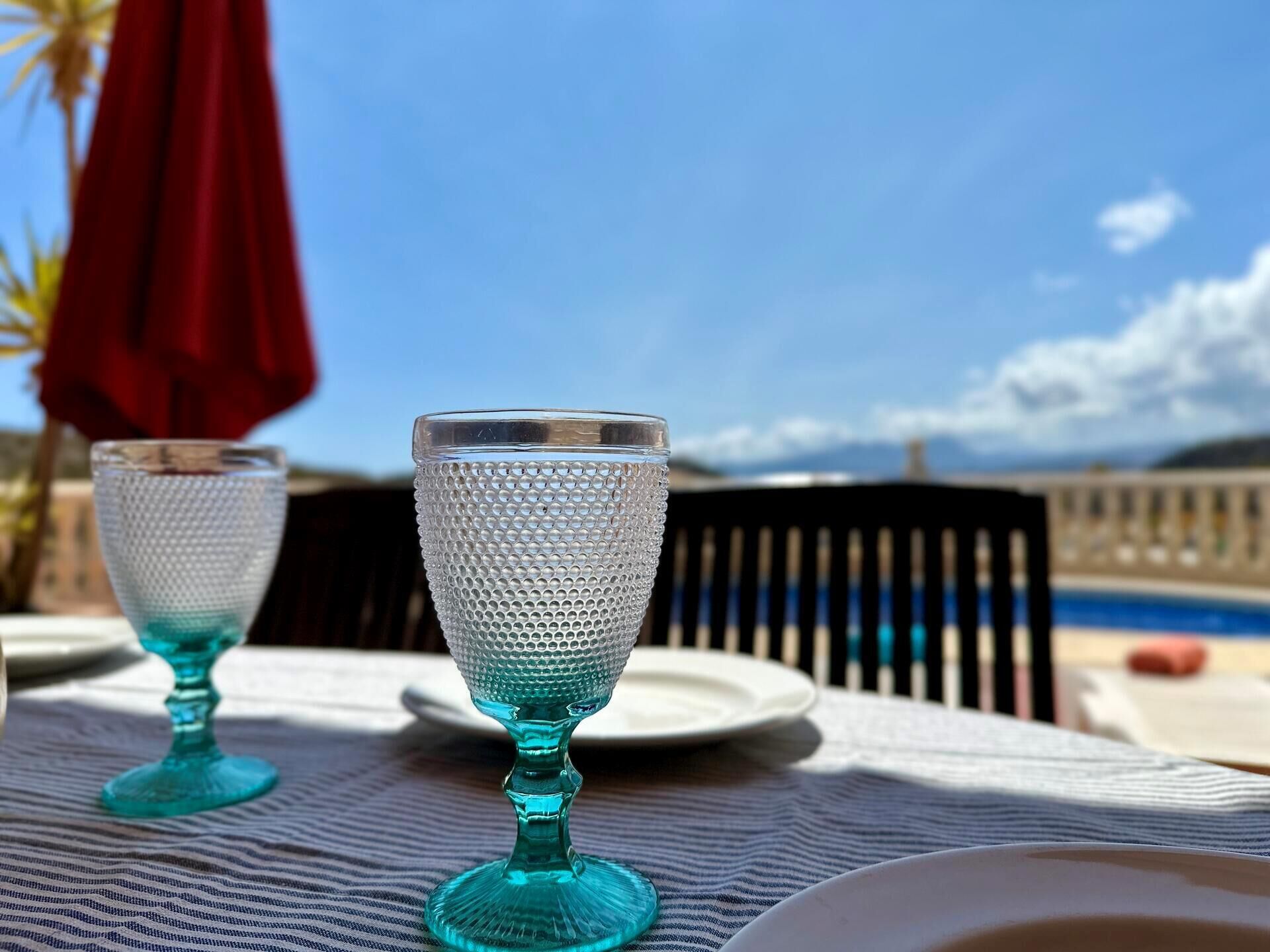 Two glass tumblers on a table with a view of a pool and mountains in the background.