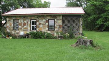Charming stone house with a red roof, surrounded by a lush garden and a wooden bench.