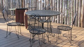 Una mesa metálica redonda con cuatro sillas, un banco y una terraza de madera.