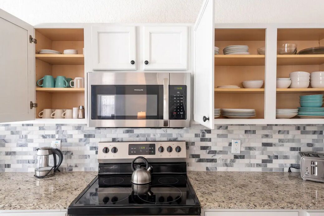A modern kitchen with white cabinets, a stainless steel microwave, a gas stove, and a coffee maker.