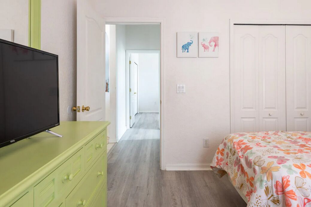 Une chambre à coucher avec un lit, un téléviseur posé sur une commode verte, un couloir et une porte donnant sur une autre pièce.
