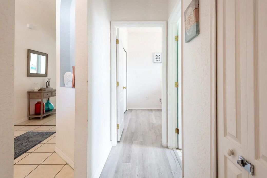 A narrow hallway with a light-colored floor, a wooden bench with a red container, and a framed picture on the wall.
