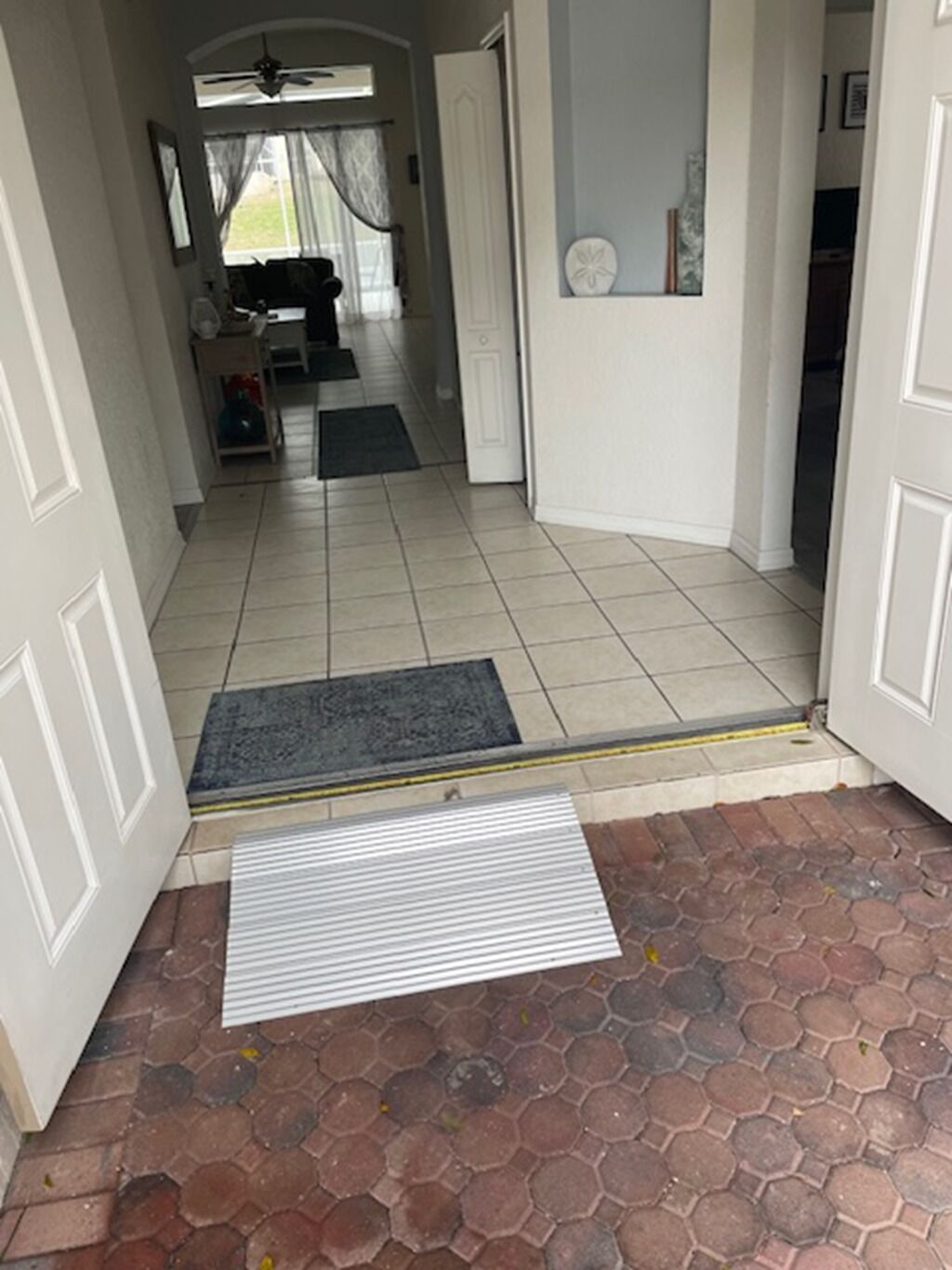 Un pasillo con suelo de baldosas que conduce a una habitación con ventilador de techo y ventana con cortinas.