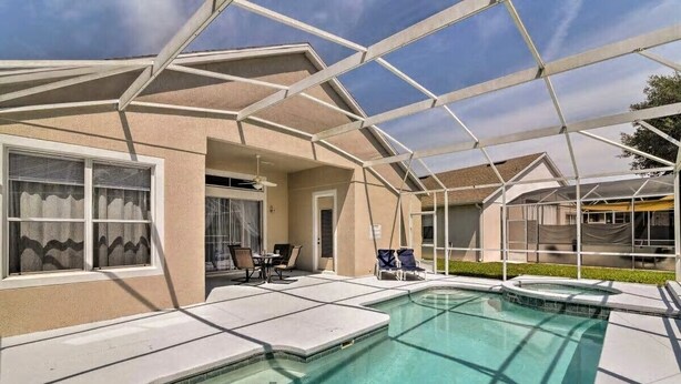 Ein Schwimmbecken mit Glasumrandung, eine überdachte Terrasse und der Blick auf ein Haus.
