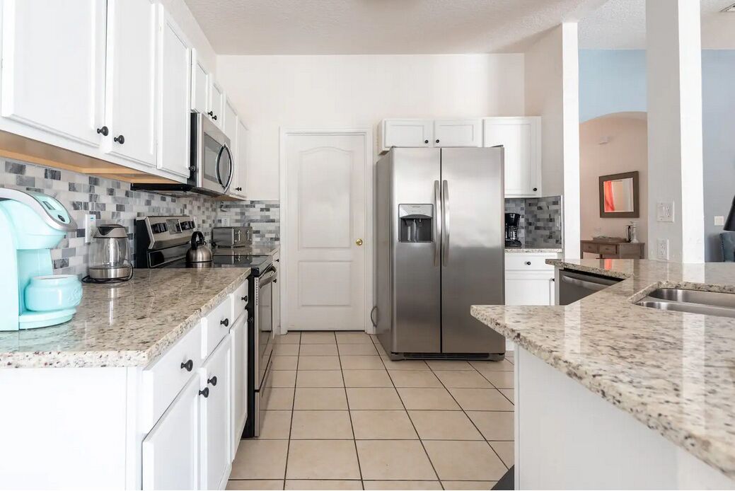 A modern kitchen with white cabinets, a stainless steel refrigerator, a microwave, and a coffee maker.