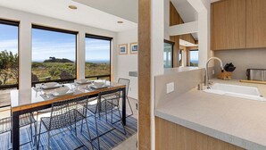 Une cuisine moderne dotée d’une grande fenêtre, un coin repas avec une table dressée pour quatre personnes, et une vue sur le paysage.