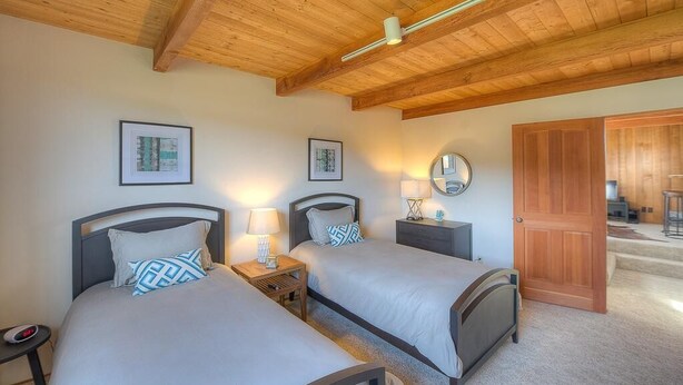Une chambre d’hôtel avec deux lits, des poutres en bois au plafond, des œuvres d’art encadrées accrochées aux murs et une porte en bois.