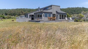 Une maison moderne avec un toit plat, de grandes fenêtres et un patio aménagé avec du mobilier d’extérieur.