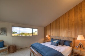 A bedroom with a large bed, two bedside lamps, a bench, a window with a view, and wooden paneling on the wall.