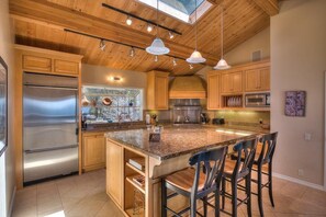 A kitchen with a large island, wooden cabinets, stainless steel appliances, and pendant lighting. - Saltwater Serenity Lodge | Hot Tub & Views (Sea Ranch)