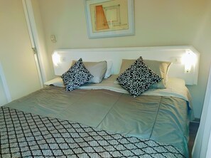 A neatly made bed with patterned pillows, a framed artwork above, and a simple bedside lamp. - Ninety Flat (São Paulo)