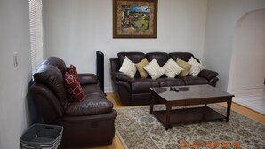 Un salon avec deux canapés en cuir marron, une table basse en bois, un tapis à motifs et un tableau encadré accroché au mur.