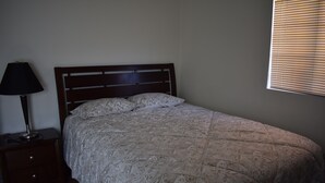 Une chambre à coucher avec un lit, une table de chevet, une lampe et une fenêtre avec des stores.