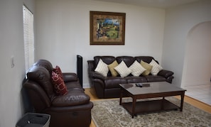 A living room with two brown leather sofas, a wooden coffee table, a patterned rug, and a framed painting on the wall.