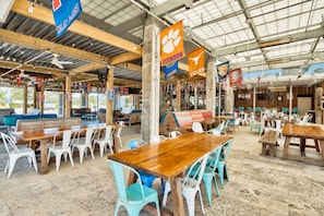 An indoor dining area with multiple wooden tables and chairs, some with colorful cushions.