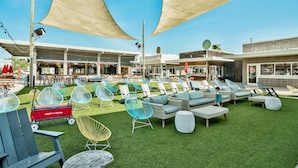 An outdoor seating area with various chairs and a dining table, surrounded by buildings with shops and a sign that reads "LUB SHOP".