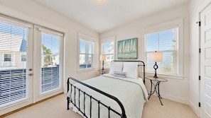 A bedroom with a bed, two bedside tables, a painting, and a view through the windows.