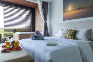A neatly made bed with a book, a tray with fruit and juice, and a view of the outdoors through large windows. - Solmare Apartments & Suites (Akumal)