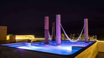 A pool area with illuminated pillars and a hammock.