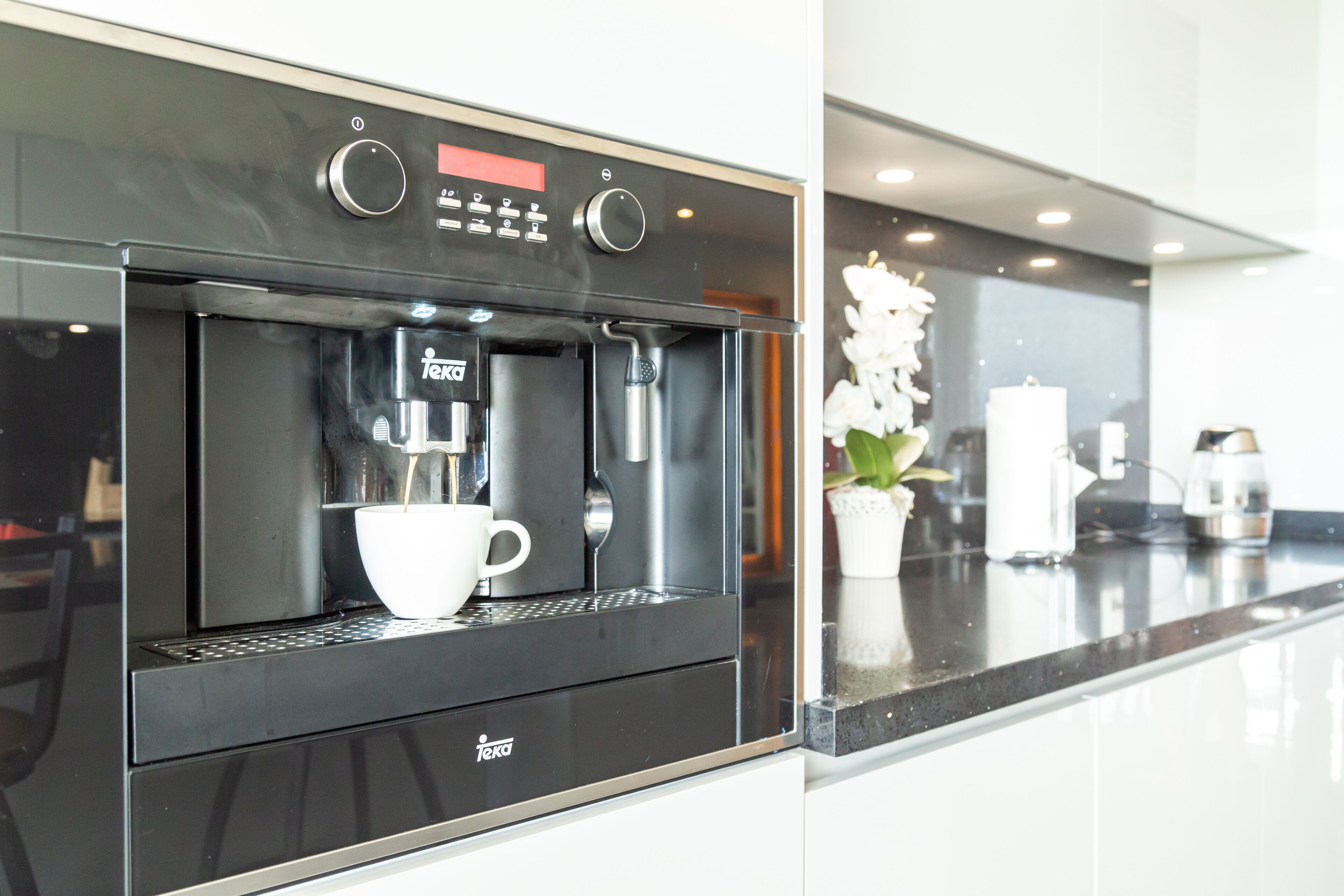 Una cucina moderna con macchina per espresso integrata, una tazza bianca e una pianta in vaso.