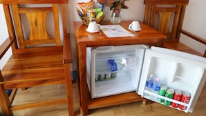 A compact dining area with a small refrigerator stocked with beverages, a bowl of snacks, and a vase with a plant. - Phong Nha Friendly Home 2 (Phong Nha)