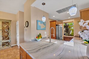 A modern kitchen with a marble countertop, stainless steel appliances, and a view to a balcony. - Molokai views, refreshed upgrades, relax comfort (Lahaina)
