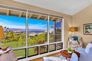 A room with large windows, a view of the ocean, a sofa, a lamp, and a framed picture on the wall. - Molokai views, refreshed upgrades, relax comfort (Lahaina)