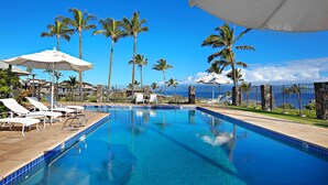 A swimming pool with lounge chairs and umbrellas, surrounded by palm trees and a view of the ocean. - Molokai views, refreshed upgrades, relax comfort (Lahaina)