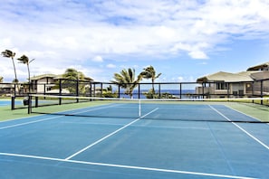 Una cancha de tenis con red, rodeada de palmeras y vista al océano.