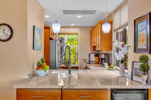 A modern kitchen with a marble countertop, stainless steel appliances, wooden cabinets, and pendant lighting. - Molokai views, refreshed upgrades, relax comfort (Lahaina)
