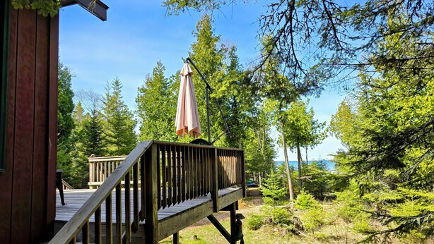 A wooden deck leading to a cabin with a view of a forest and a body of water.