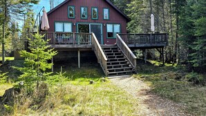 A cabin with a wooden deck, a staircase, and a view of the surrounding forest.