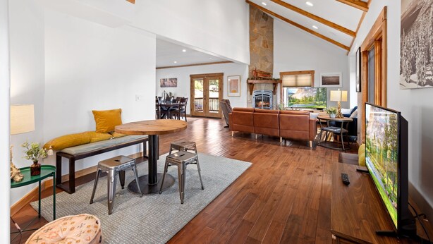 A spacious living room with a wooden floor, a fireplace, a large TV, and a dining area with a table and chairs.