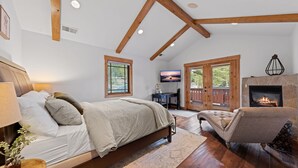 A bedroom with a bed, a desk, a television, and a fireplace.