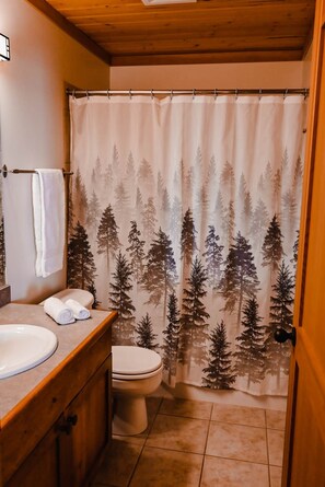 Un baño con tocador de madera, inodoro y cortina de ducha con estampado de bosque.