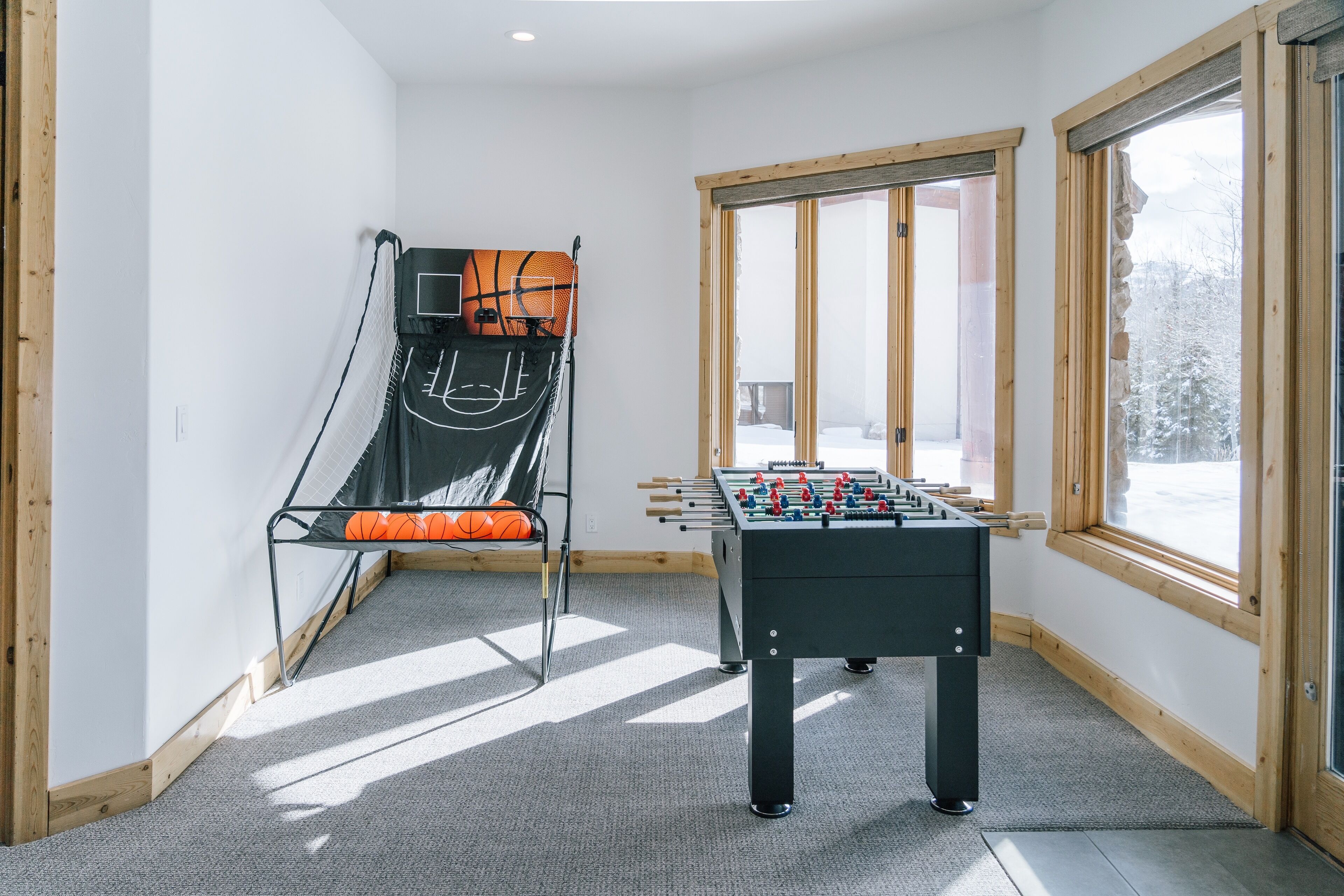 Ein Zimmer mit Kicker, Trampolin und großen Fenstern mit Blick auf Bäume.