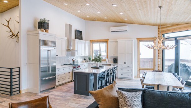 Une cuisine spacieuse avec des meubles blancs, un îlot central et un coin repas comprenant une table et des chaises en bois.