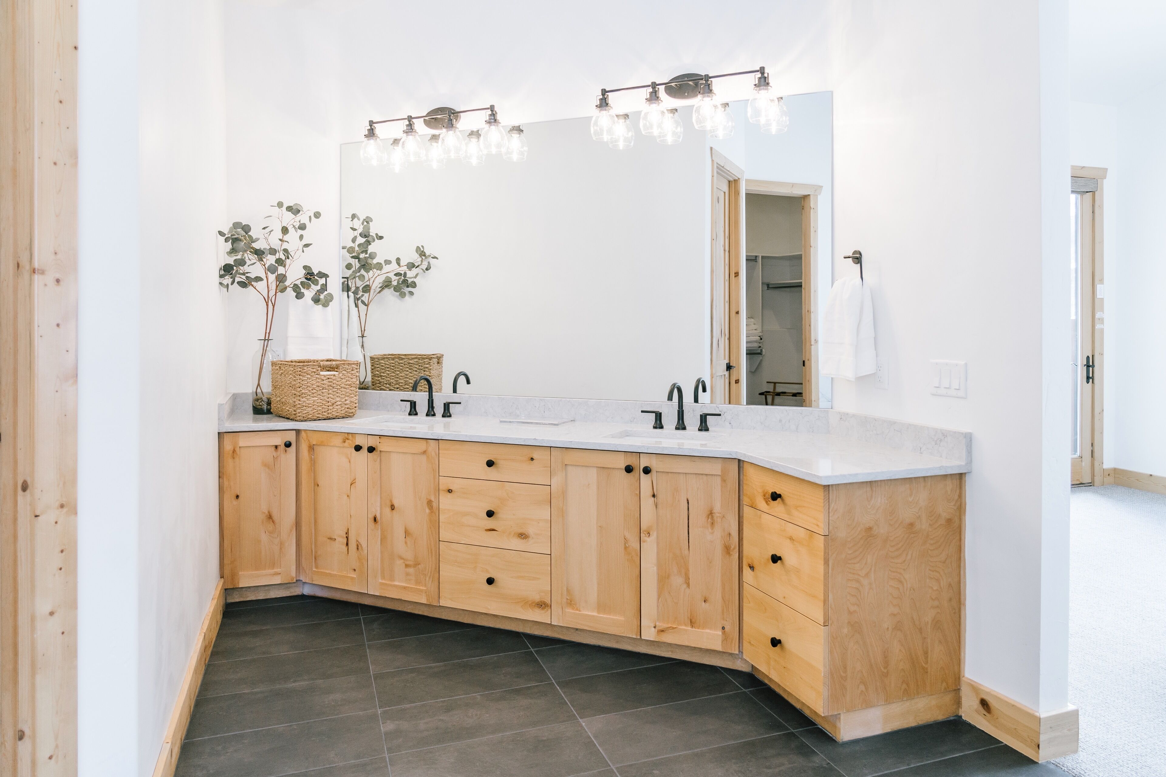 A modern bathroom with a large mirror, wooden cabinets, and a white countertop.