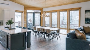 Une cuisine moderne dotée d’un grand îlot central, d’un plafond en bois et de grandes fenêtres offrant une vue sur l’extérieur.